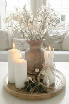 three white candles sitting on top of a wooden tray next to a vase filled with flowers