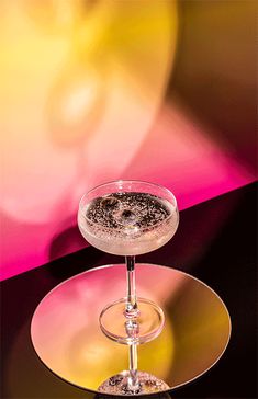 a glass filled with liquid sitting on top of a white and gold plate next to a pink background