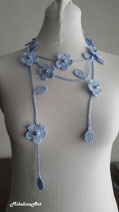 a white mannequin with blue crocheted flowers on it's neck