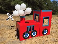 a red and blue train birthday decoration in the middle of a field with white balloons