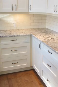 a kitchen with white cabinets and marble counter tops