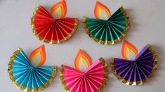 four colorful paper fan decorations on a white table with gold trimmings and red, green, blue, yellow, and orange colors