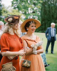 two women in orange dresses and hats standing next to each other on a grass field