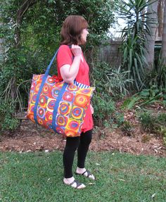 a woman carrying a colorful handbag on her shoulder while standing in front of some bushes