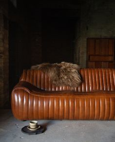 a brown leather couch with a furry pillow on it's back and the seat up