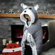 a child wearing a crocheted animal hat and scarf in front of a fireplace