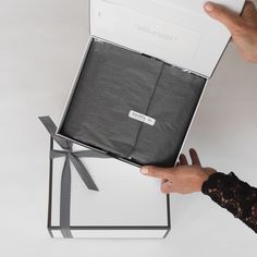 a person is holding an open box with black fabric and ribbon on the inside, while another hand holds it in front of them