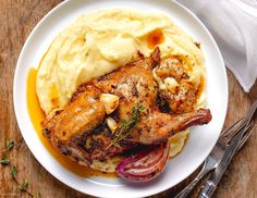 a white plate topped with meat and mashed potatoes on top of a wooden table