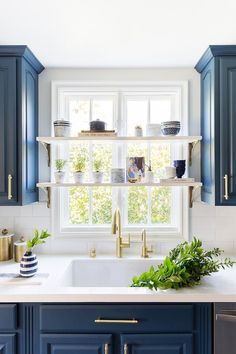 a kitchen with blue cabinets and gold pulls on the window sill above the sink