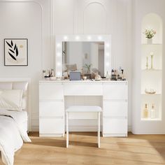 a bedroom with white furniture and lights on the mirror above the dresser, along with a bed