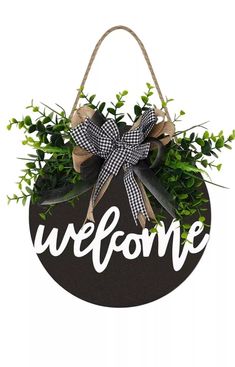 a welcome sign hanging from the side of a wooden plaque with greenery in it