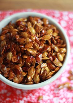 a white bowl filled with pumpkin seeds on top of a red and white table cloth