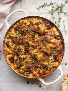 a casserole with meat and cheese in a white dish on a table next to bread