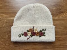 a white beanie with flowers on it sitting on top of a wooden table next to a pair of scissors