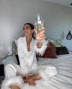 a woman sitting on top of a bed holding a wine glass in one hand and smiling at the camera