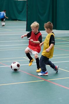 two young boys playing soccer on an indoor court