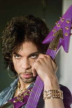 a man holding a purple guitar in his right hand and looking at the camera with an intense look on his face