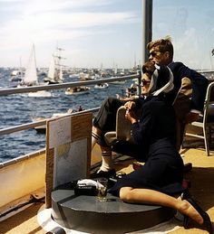 two people sitting on a boat looking at the water and boats in the ocean behind them