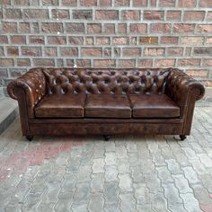 a brown leather couch sitting in front of a brick wall