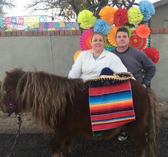 a man and woman standing next to a small horse with a mexican blanket on it's back