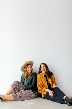 two women sitting next to each other on the floor laughing and posing for a photo