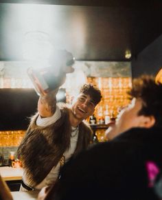 a man holding up a clock above his head in front of other people at a bar