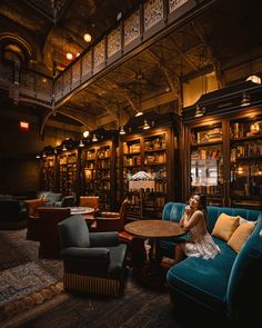 a woman sitting at a table in a library filled with lots of books and furniture