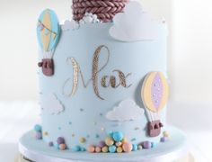 a blue cake decorated with hot air balloons and the word max on it's side