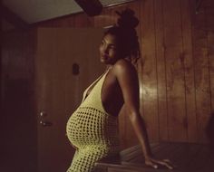 a pregnant woman in a yellow dress leaning on a wooden bench with her hand on her hip