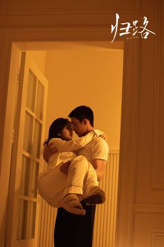 a man and woman embracing each other in front of an open door with chinese characters on the wall