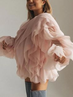 a woman wearing a pink top with ruffles on the shoulders and arms, smiling