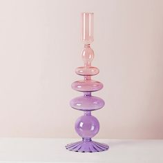 a tall purple glass candle holder sitting on top of a white table next to a pink wall