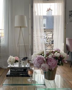 a living room filled with furniture and flowers on top of a coffee table in front of a window