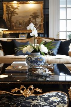 a living room filled with furniture and flowers on top of a coffee table in front of a painting