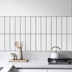 a kitchen with white tiles and wooden utensils on the counter top, next to a stove