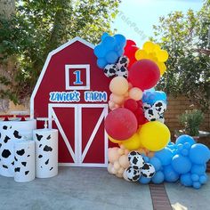 a bunch of balloons are in front of a red barn with a cow print on it