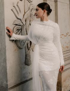 a woman in a white wedding dress leaning against a wall with her hand on the side