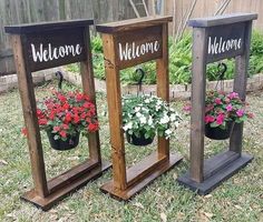 three wooden planters with flowers in them on the grass and one has a welcome sign