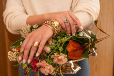 a woman is holding a bunch of flowers in her hands with gold rings on their fingers