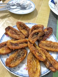 there is a plate full of fried bananas on the table with forks and spoons