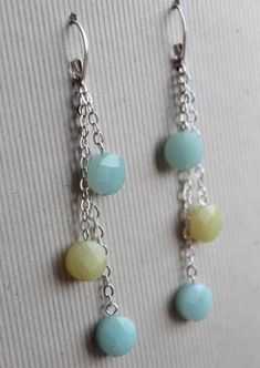 two pairs of blue and yellow beads hanging from silver chain earring hooks on a white surface