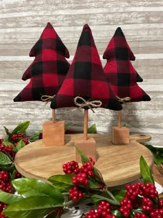 three red and black christmas trees sitting on top of a wooden board next to berries