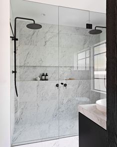 a bathroom with a glass shower door and white marble counter top, along with a sink