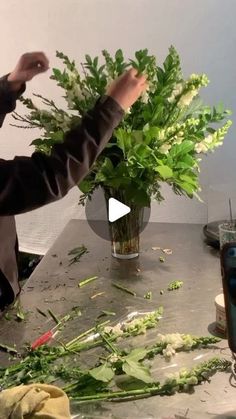 a man is making flowers in a vase on a table with other items around him