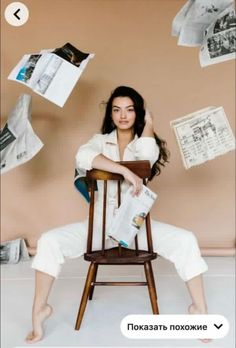 a woman sitting on top of a wooden chair next to papers flying in the air