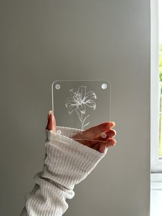 a person holding up a clear plastic object with a flower etched on the front and side