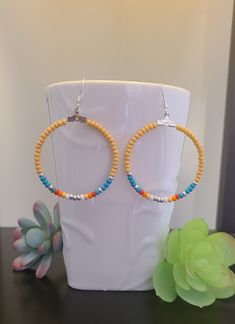 a pair of yellow and blue beaded hoop earrings sitting on top of a white vase