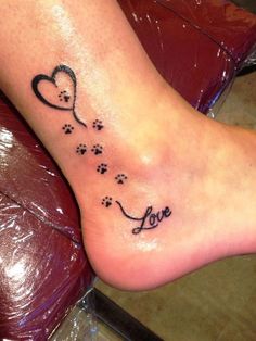 a person with a tattoo on their foot that says love and has paw prints in the shape of a heart