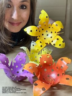 a woman is posing next to some flowers that are made out of colored plastic material