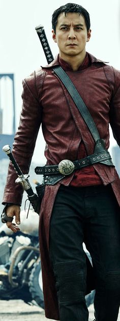 a man in a red leather outfit with two swords on his shoulder and one arm extended